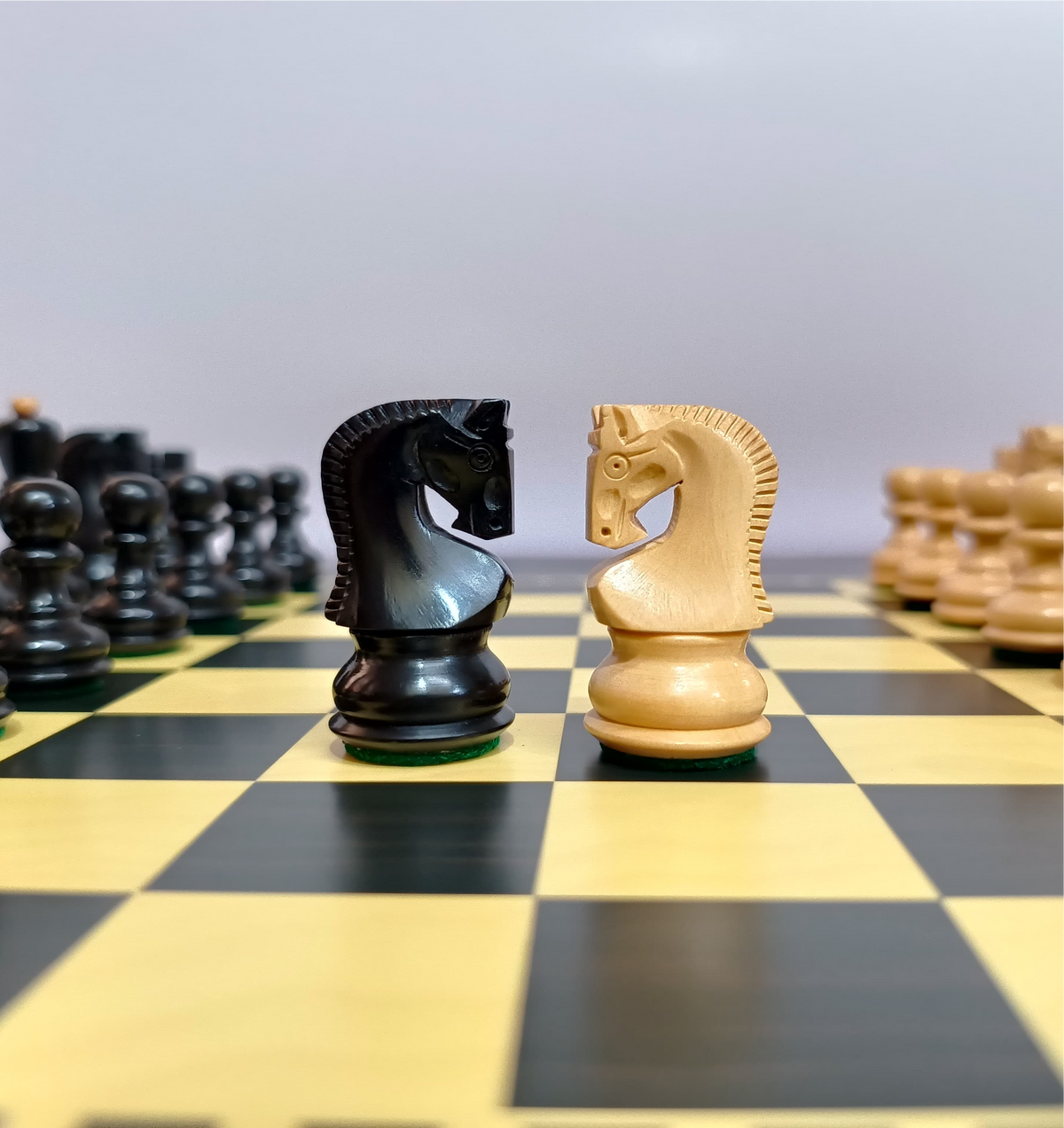Black and cream wooden chess knights facing each other on a yellow and black chessboard.
